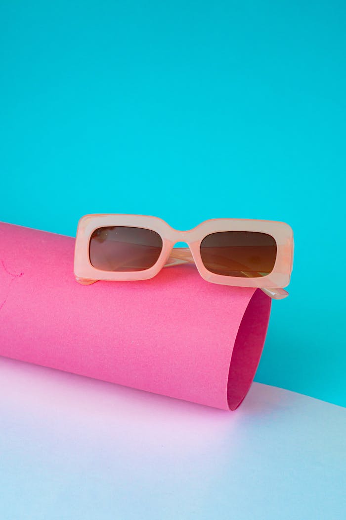 Stylish sunglasses displayed on a vibrant pink roll against a blue background, offering modern fashion vibes.