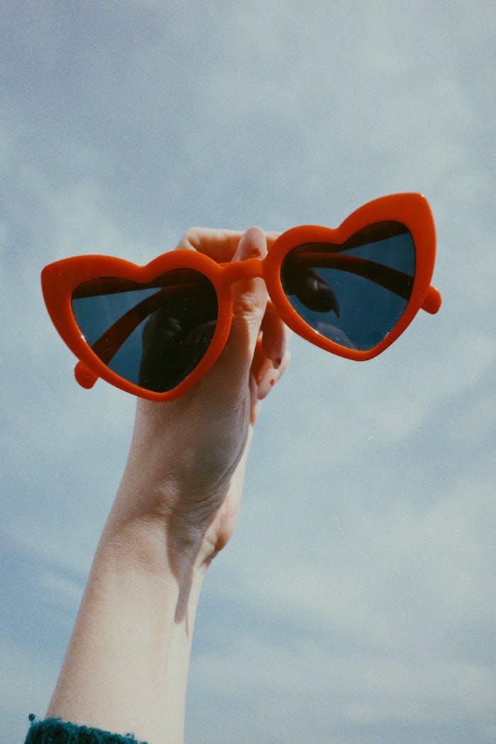 Bright red heart sunglasses against a clear blue sky. Perfect for summer vibes.